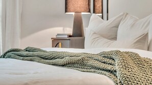 Un lit bien fait, recouvert d’une couverture verte tricotée, avec une lampe de chevet et un oreiller blanc.