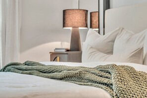 A neatly made bed with a green knitted blanket, a bedside lamp, and a white pillow. - Cozy Stay ATL -2BD/2BTH FreeParking & 5* Amenities (Atlanta)