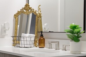 Ein Badezimmer mit einem spiegelnden, goldfarbenen Rahmen, einem Handtuchhalter, einem Seifenspender und einem Blumentopf.