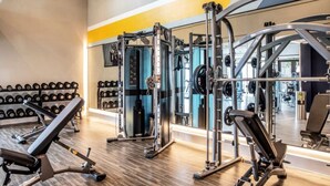 Un gimnasio con equipo de levantamiento de pesas, bancos y un espejo grande.