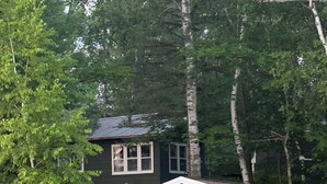 En liten, envåningsbyggnad med ett garage, omgiven av träd och en gräsyta.