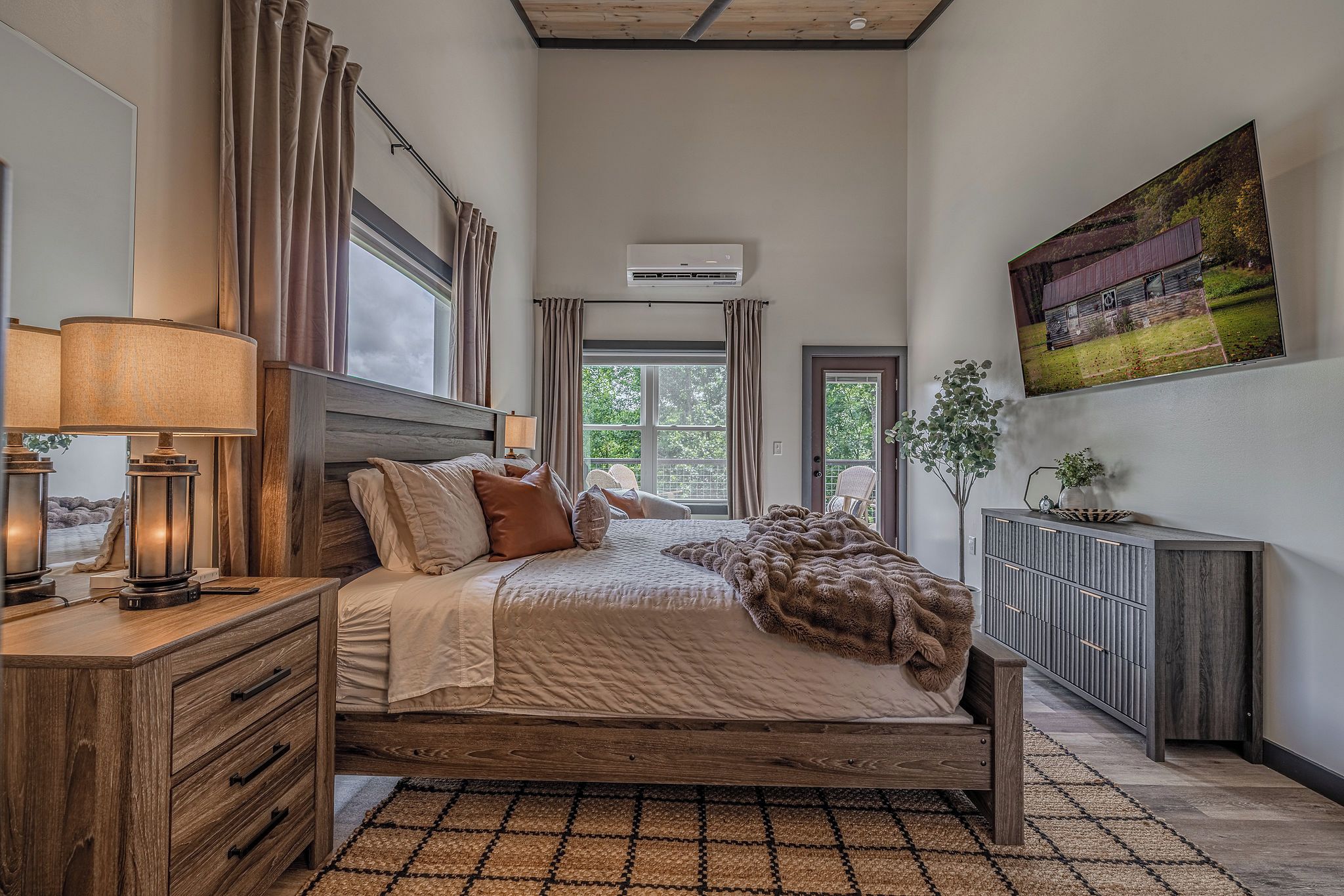 Une chambre à coucher comprenant un lit, des tables de chevet, un radiateur, une fenêtre avec des rideaux, un climatiseur fixé au mur et un grand tableau.