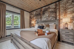 A bedroom with a large bed, wooden headboard, bedside tables, and a view of trees through a window.
