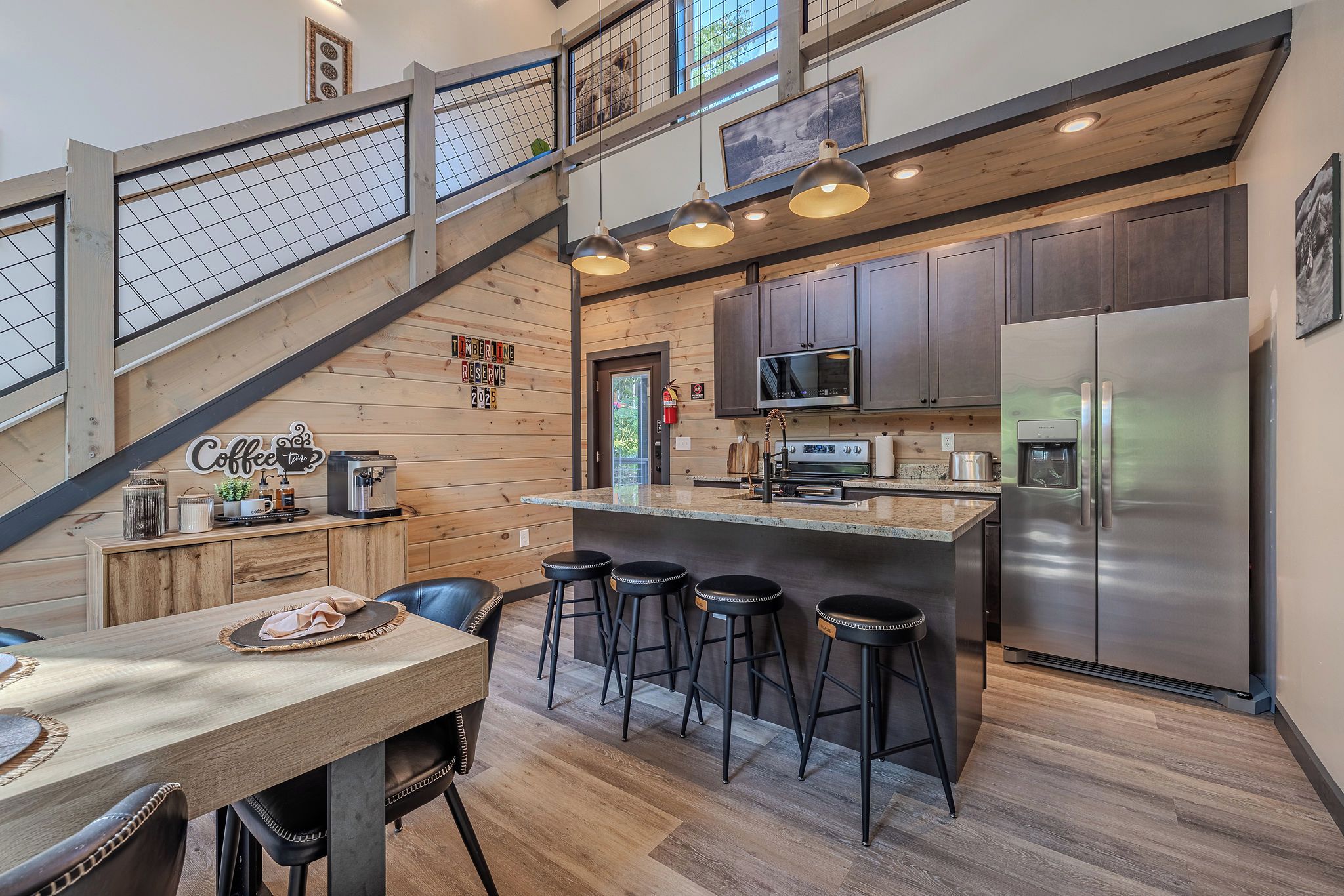 A modern kitchen with a central island, bar stools, and a staircase leading to an upper level.