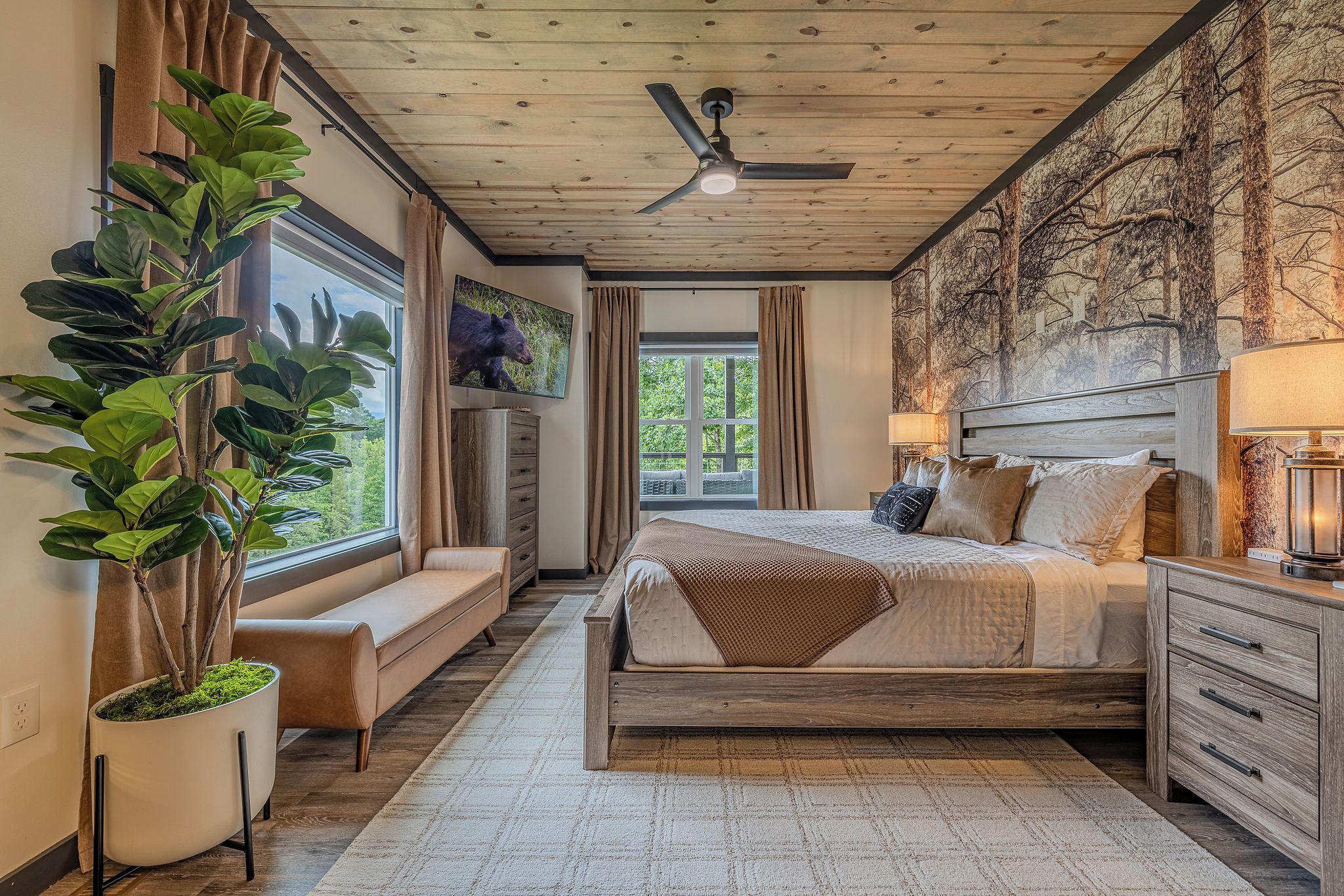 A bedroom with a large bed, a ceiling fan, a window with curtains, a plant, and a wall with a forest mural.