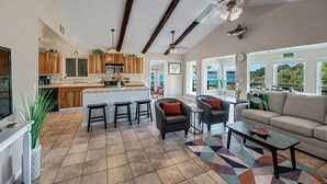 A spacious living area with a kitchen, a dining area with stools, and a sofa. There is a large window providing a view of the outdoors. - BoGi - 3/2 Canyon Lake Waterfront + Sweeping Lake Views Off Multiple Decks + Ping Pong + Games (Canyon Lake)