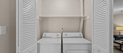A laundry room with two stacked washers and dryers, a vent, and a power outlet on the wall.