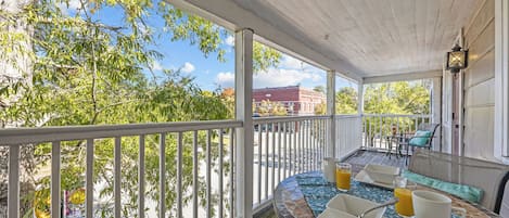 A covered porch with a table set for breakfast, a chair, and a view of trees and a building in the background.