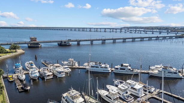 Un puerto deportivo con varias embarcaciones amarradas, un puente al fondo y una pequeña isla con un edificio.
