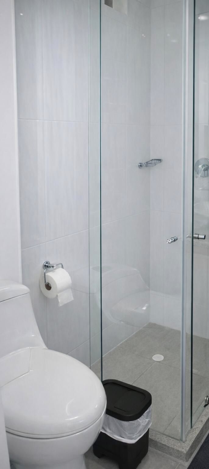 Une salle de bain comprenant des toilettes, une douche à parois de verre et une poubelle.