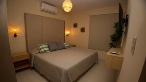 Une chambre à coucher comprenant un lit, des tables de chevet, un climatiseur, des lampes fixées au mur et un téléviseur.