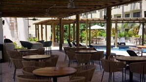 Un espace extérieur aménagé avec une terrasse, des tables et des chaises en osier, une piscine et un coin salon abrité.
