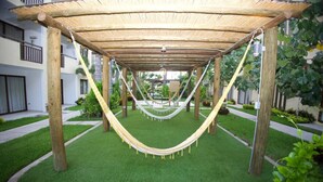 Un hamac sous une pergola en bois, dans un jardin bien entretenu, offrant une vue dégagée sur les bâtiments environnants.