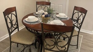 A dining area with a round table, four chairs, a chandelier, and a mirror on the wall.
