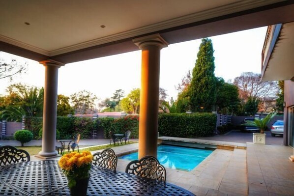 A covered patio area with a pool, outdoor furniture, and a view of the surrounding landscape. - Jade Garden Guest House (Sandton)