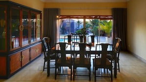 A dining area with a large table and chairs, a cabinet with glass doors, and a view of a pool and greenery outside.