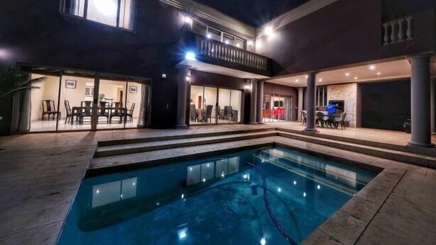A swimming pool with a covered patio area, a dining area with tables and chairs, and a building with multiple windows and balconies.