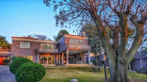 A two-story house with a balcony, a well-maintained lawn, and a large tree.