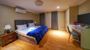 A hotel room with a bed, bedside table, lamp, desk, chair, and a television.
