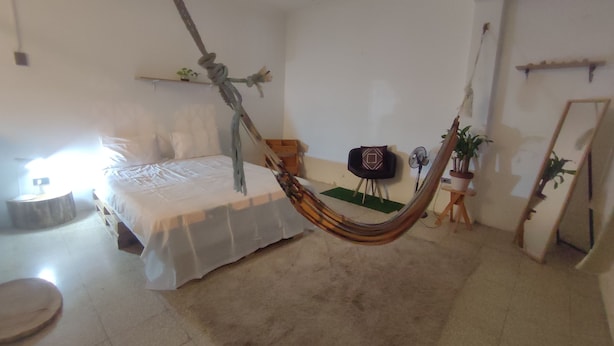 A bedroom with a hammock, a bed, a small table, a chair, a mirror, and a potted plant. - Pachamac House (Guayaquil)