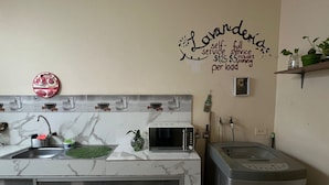A kitchen with a marble backsplash, a sink, a microwave, a toaster, and a refrigerator. There is a wall decoration with text and a small plant on the countertop. - Pachamac House (Guayaquil)