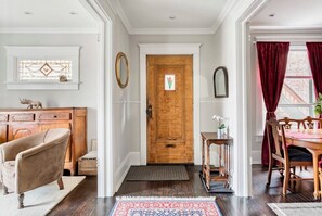 A hallway with a wooden door, a bench, a small table with a plant, and a dining area with a table and chairs.