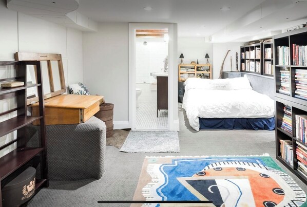 A bedroom with a bed, a desk, a bookshelf, and a rug.