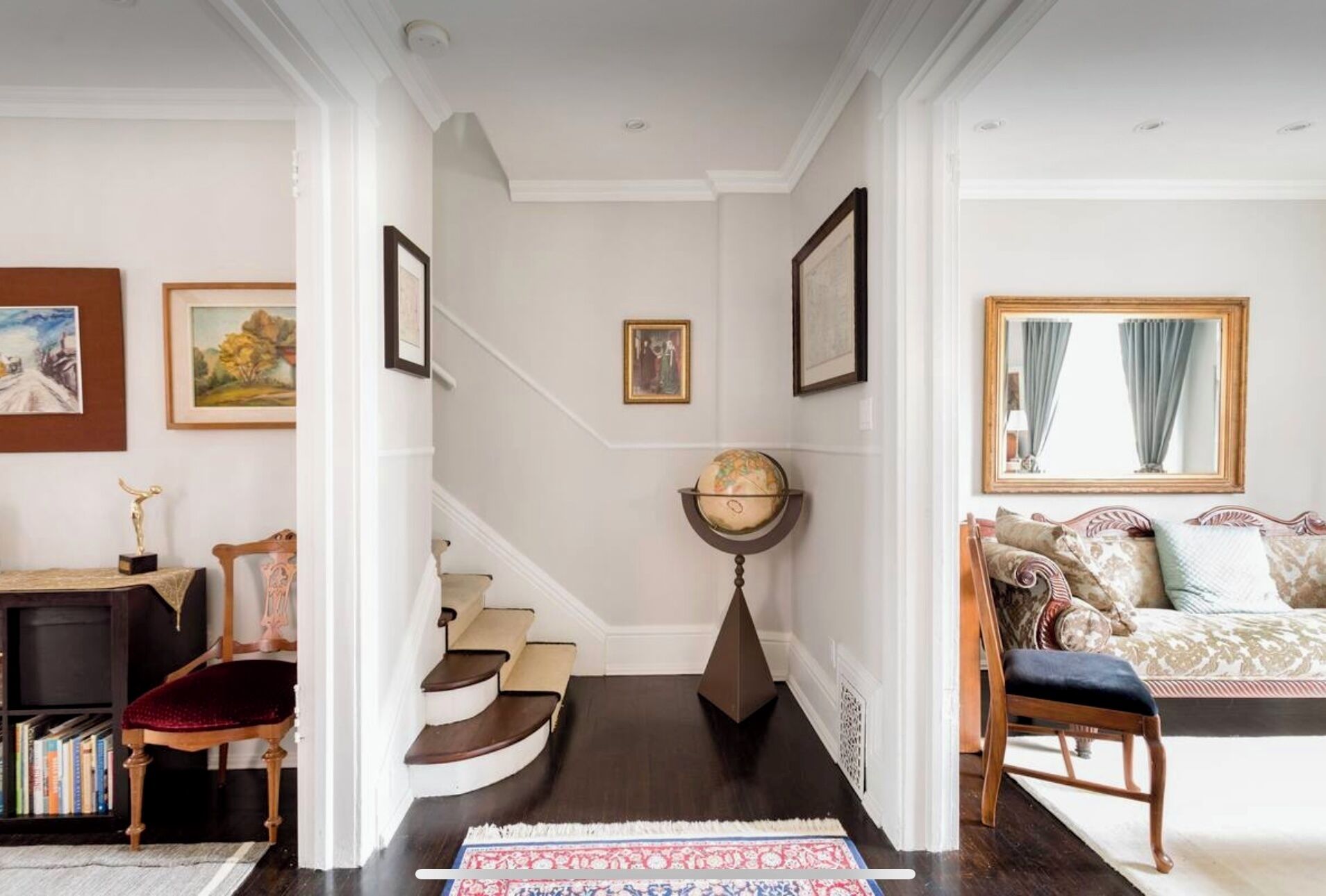 A staircase with a globe, framed artwork, and a sofa with patterned cushions.