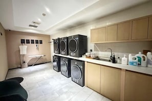 Une buanderie équipée d’une machine à laver et d’un sèche-linge superposés, d’un étendoir et d’un évier avec des produits de toilette.