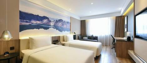 A hotel room with two beds, a desk, a large window, and a mountain landscape mural.