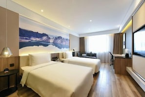 Une chambre d’hôtel avec deux lits, un bureau, une grande fenêtre et une fresque murale représentant un paysage de montagne.