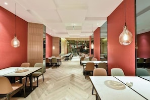 A modern restaurant interior with wooden flooring, red walls, and hanging pendant lights. Tables are arranged in a linear fashion with chairs. - Atour Hotel(Beijing Chaoyang Park Red Scarf Bridge) (Beijing)