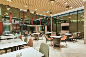 Een moderne eetruimte met tafels, stoelen, een houten plafond en grote ramen.
