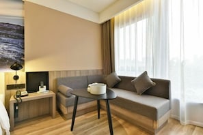 A modern hotel room with a sofa, a small table, a lamp, and a painting on the wall. - Atour Hotel(Beijing Chaoyang Park Red Scarf Bridge) (Beijing)