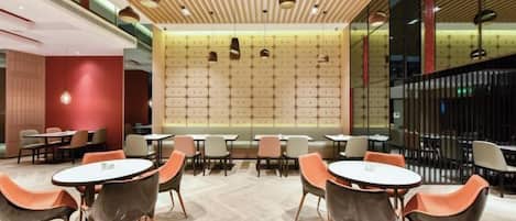 A modern interior with round tables and orange chairs, a patterned wall, and a wooden ceiling.