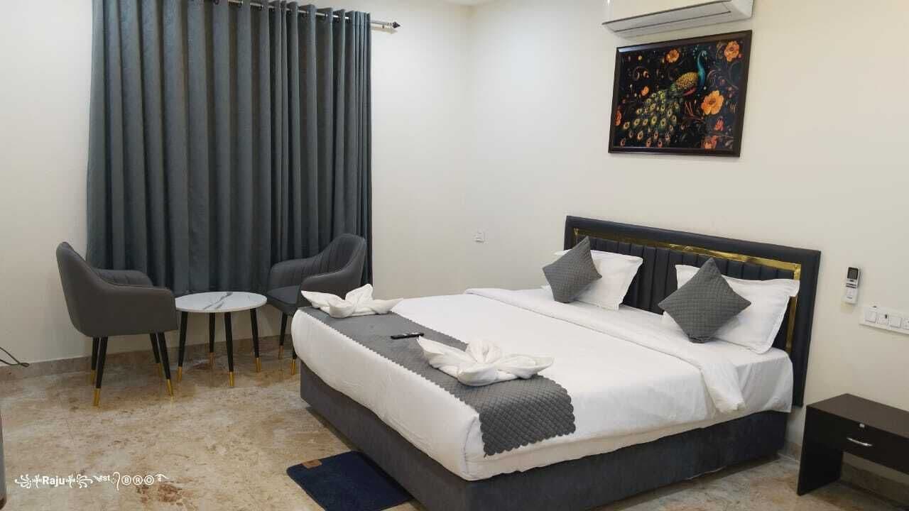 A neatly arranged bedroom with a bed, two chairs, a small table, and a painting on the wall.