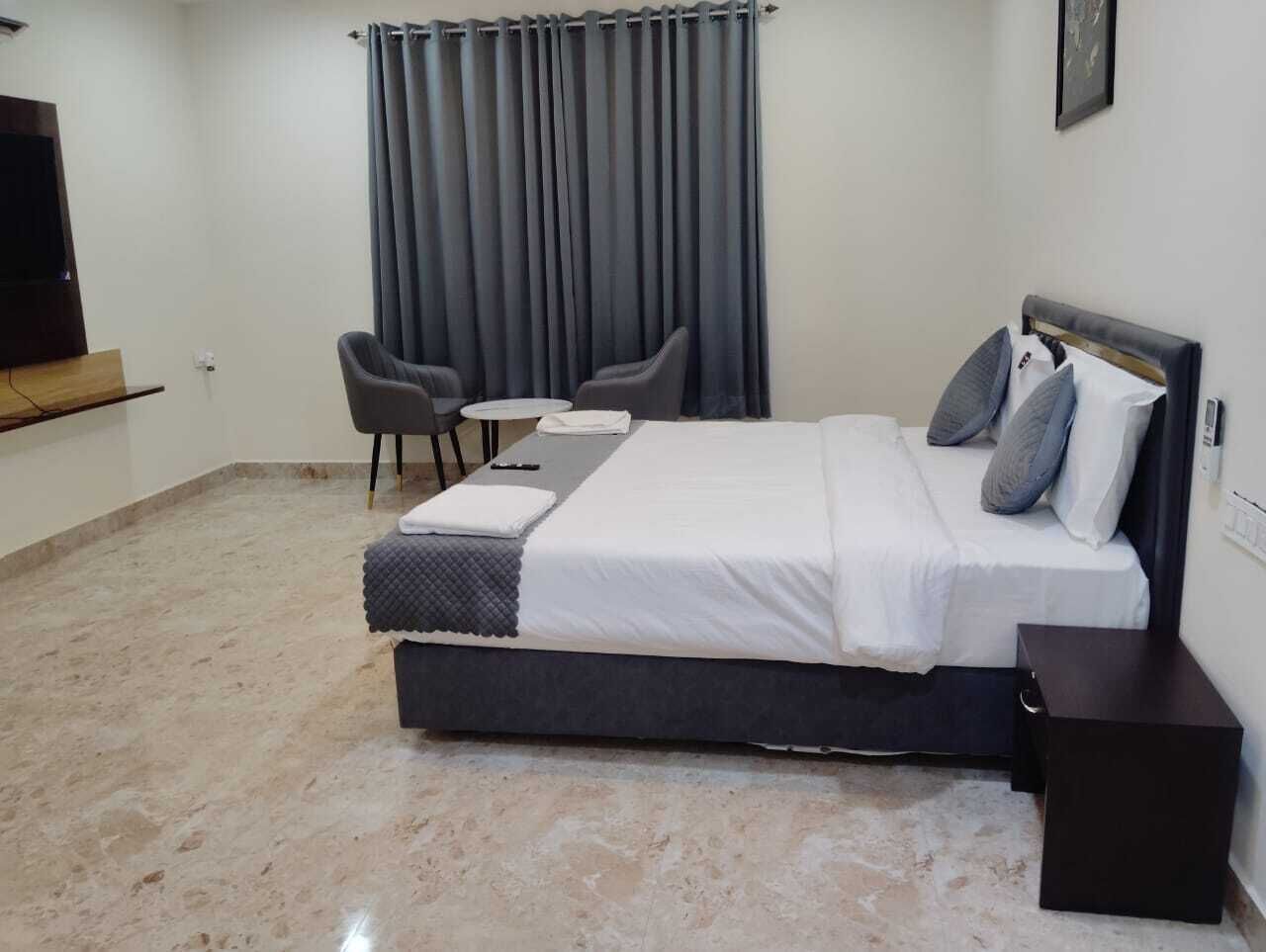 Een slaapkamer met een bed, twee stoelen, een klein tafeltje, een televisie en een gordijn.