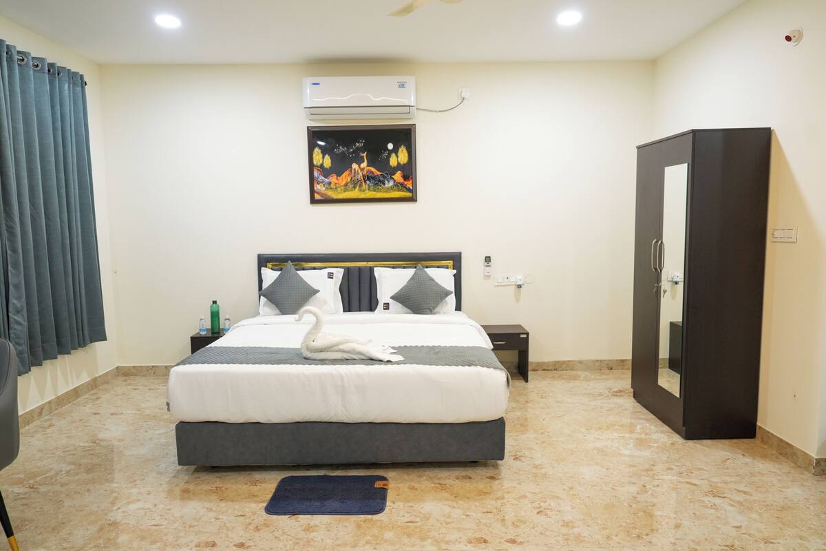 A hotel room with a bed, a nightstand, an air conditioner, a wardrobe, and a painting on the wall.