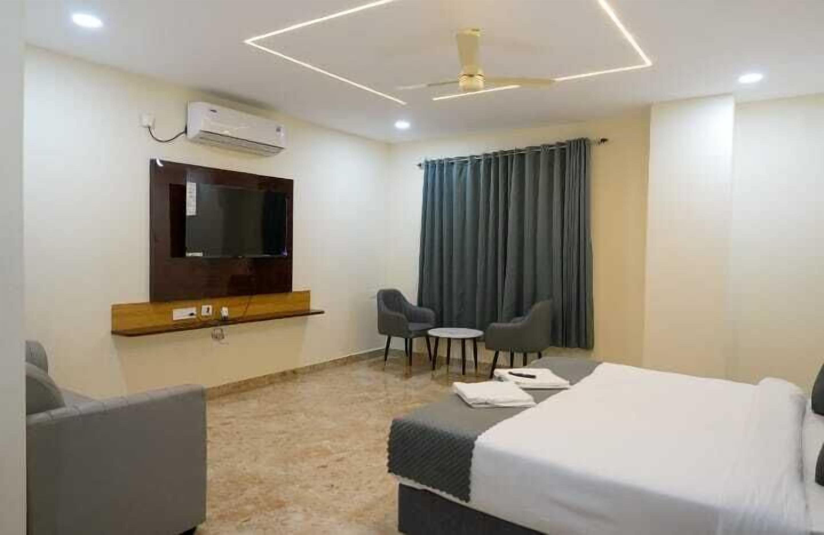 Ein Hotelzimmer mit Bett, Wandfernseher, einem kleinen Tisch mit Stühlen und einem Fenster mit Vorhängen.