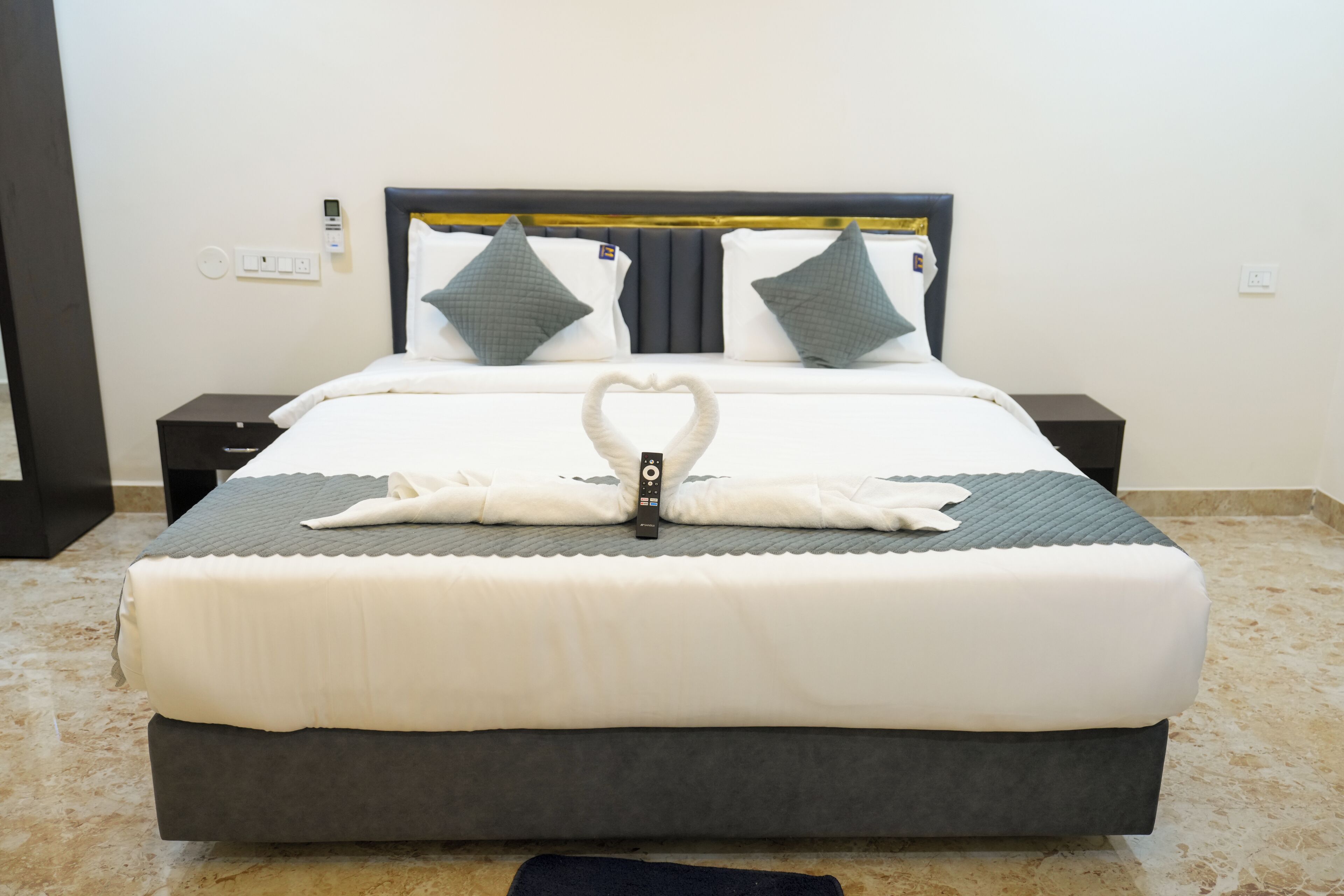 A neatly made bed with a heart-shaped towel arrangement, a control panel on the wall, and a marble floor.
