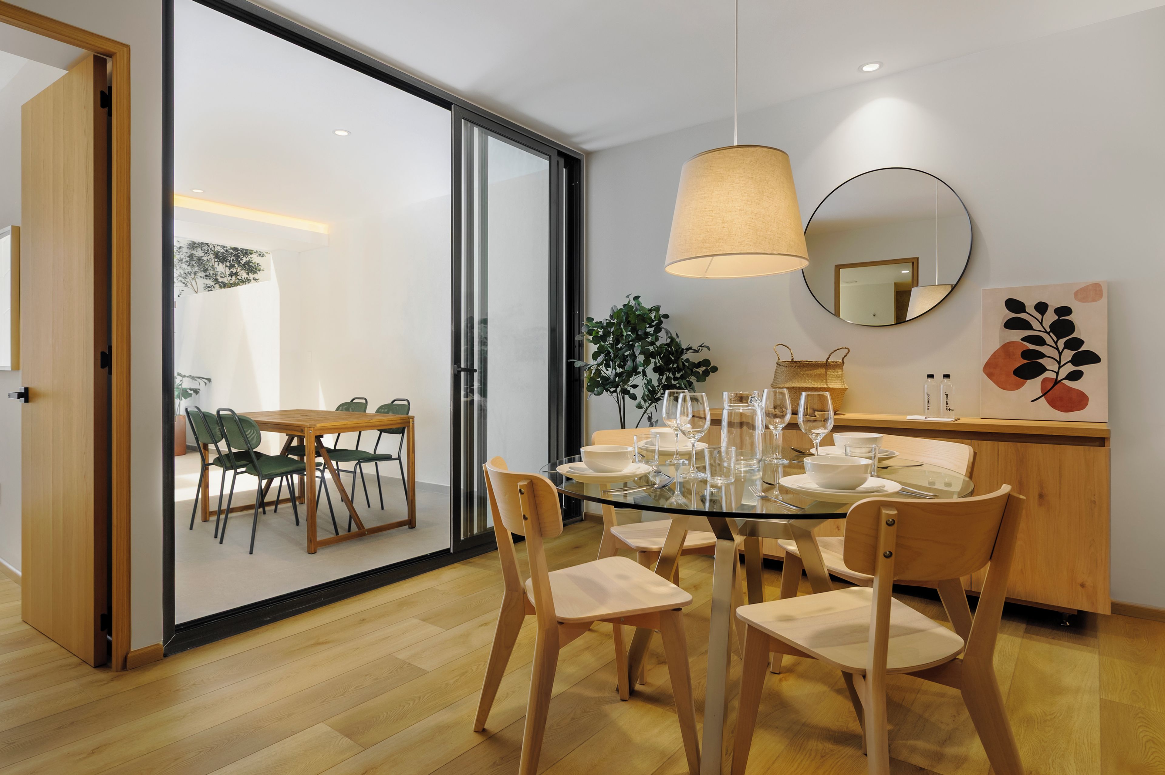 A modern dining area with a glass table, wooden chairs, and a hanging lamp.