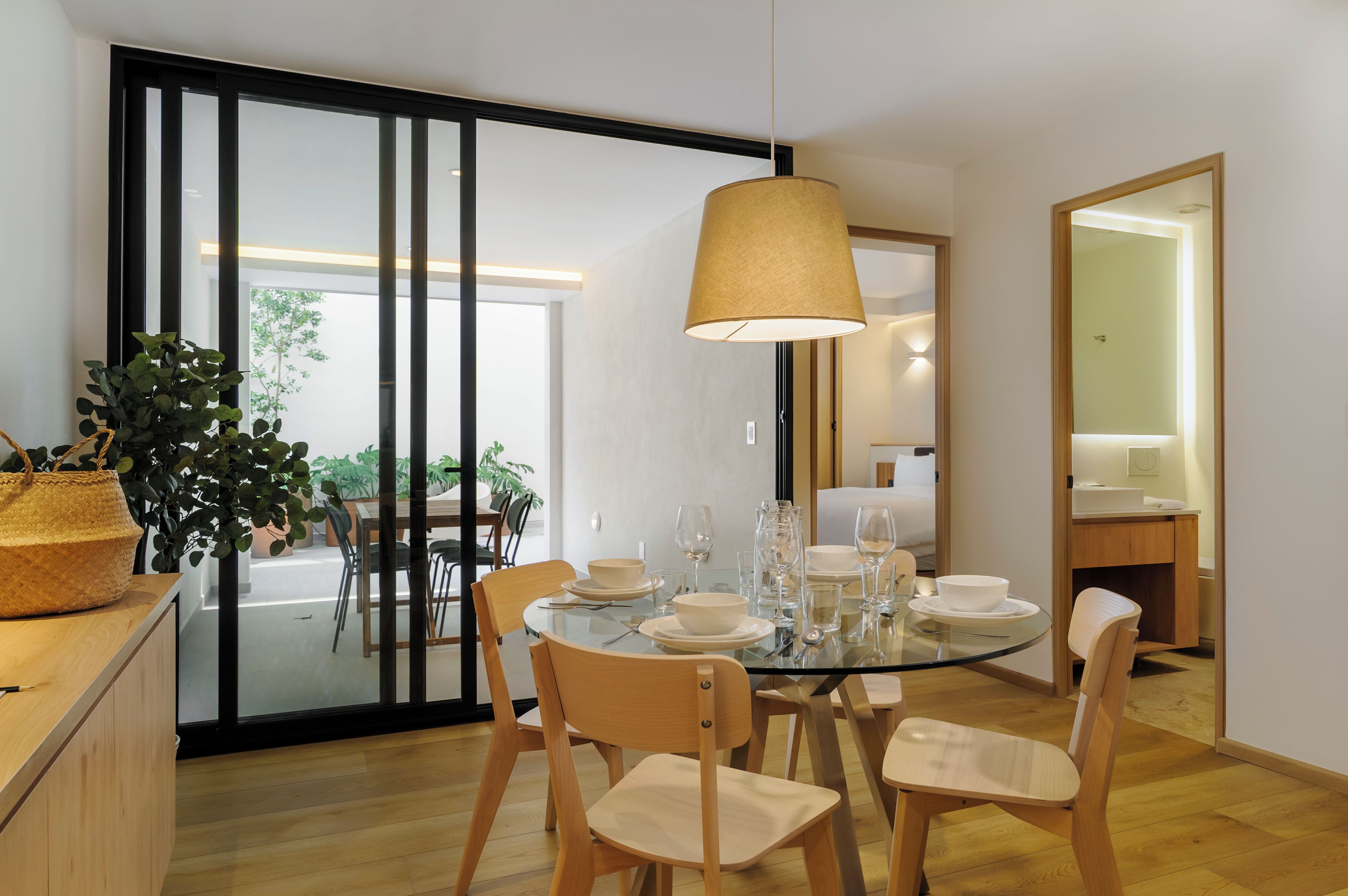 A modern dining area with a glass table, wooden chairs, and a hanging lamp.