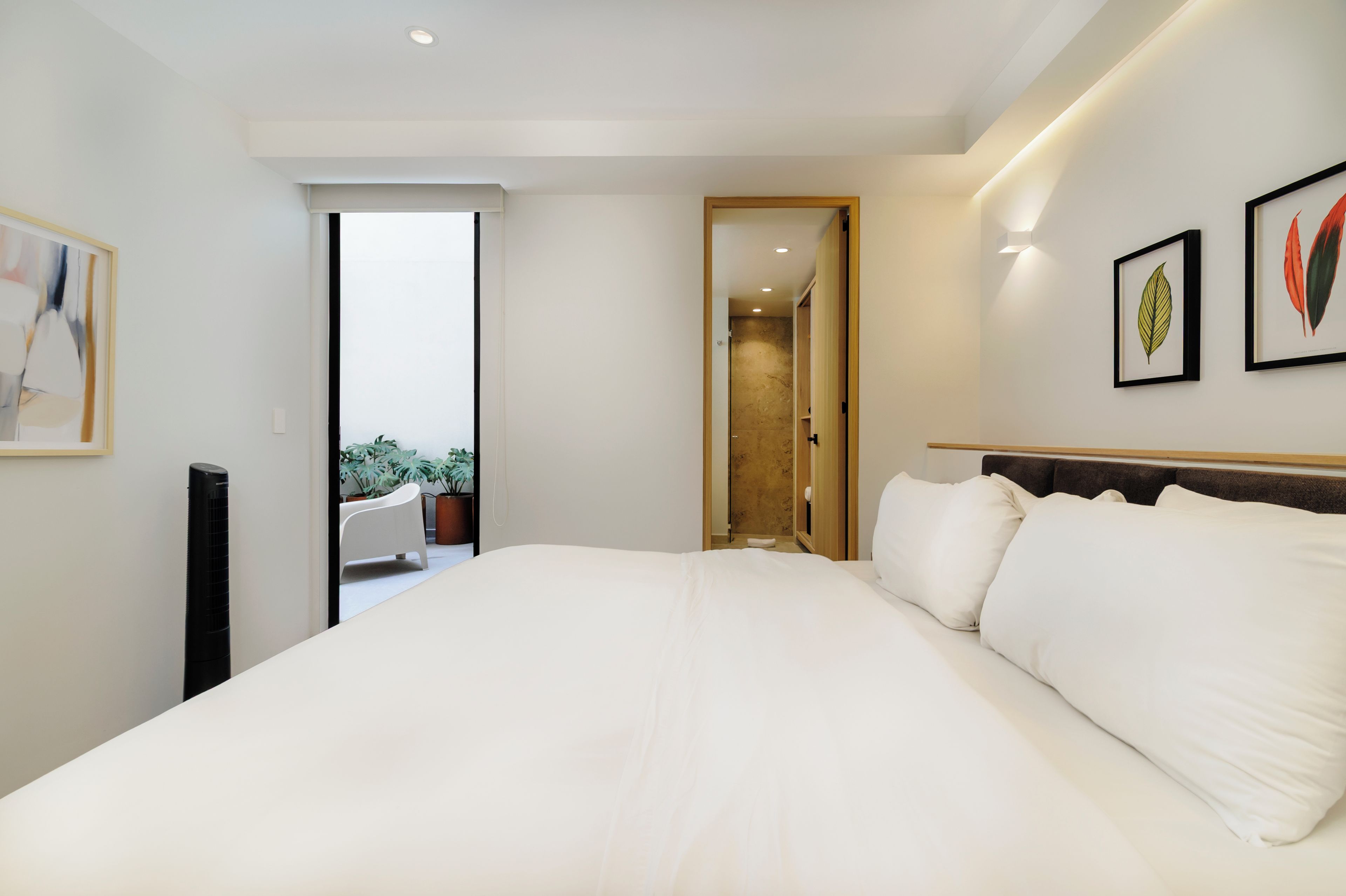 A hotel room with a large bed, a door leading to a balcony, and two framed botanical prints on the wall.