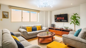A living room with a grey sofa set, a coffee table, and a TV mounted on the wall. - Esmeralda Shelter - Jacuzzi (Cuenca)