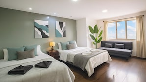 A hotel room with two beds, a sofa, a large window with curtains, and artwork on the walls. - Esmeralda Shelter - Jacuzzi (Cuenca)