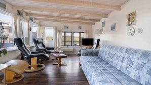 A spacious living room with a blue sofa, leather chairs, a television, and a large window with curtains. - 5 Star Holiday Home in Mesinge (Mesinge)