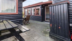 A wooden cabin with a picnic table and a chair, a small outdoor area with a bench, and a door leading to the interior. - 5 Star Holiday Home in Mesinge (Mesinge)
