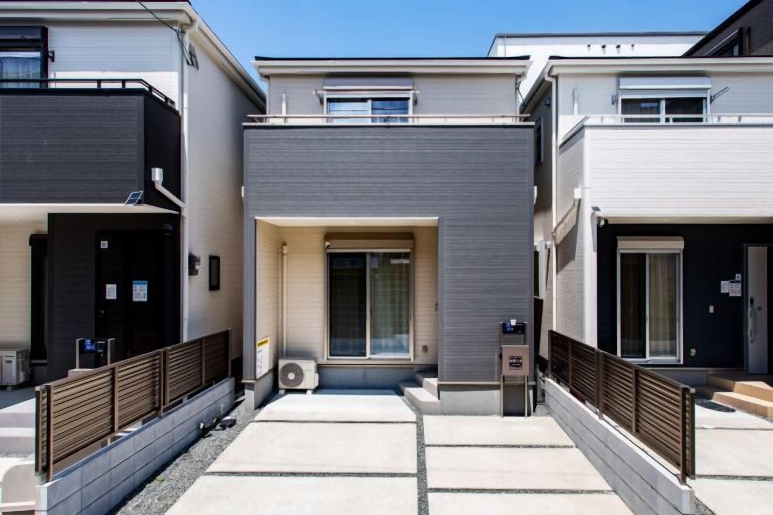 A row of modern residential buildings with balconies, a central entrance, and a small outdoor seating area.