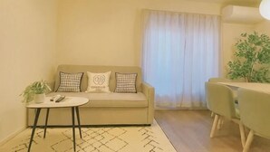 A living room with a sofa, a small table, a plant, and a dining area. - Green&Tree (Osaka)