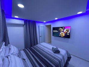 Ein Schlafzimmer mit einem Bett, Vorhängen, einem Flachbildfernseher an der Wand und einer Decke mit Einbaulampen.